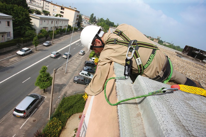 Man woking at height on a roof wearing a white helmet and in a harness