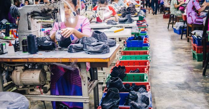 Woman making shoes using a sewing machine in a factory