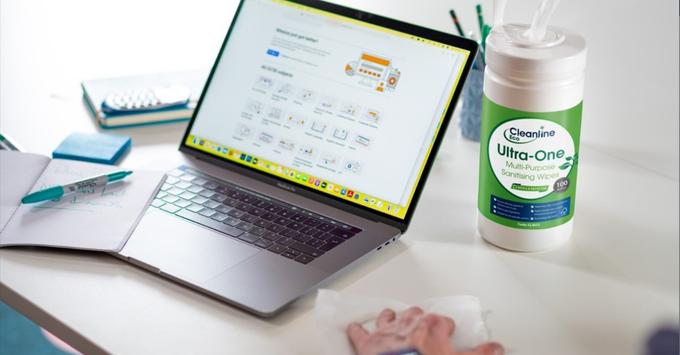 Wipes being used to clean a desk with a laptop on 