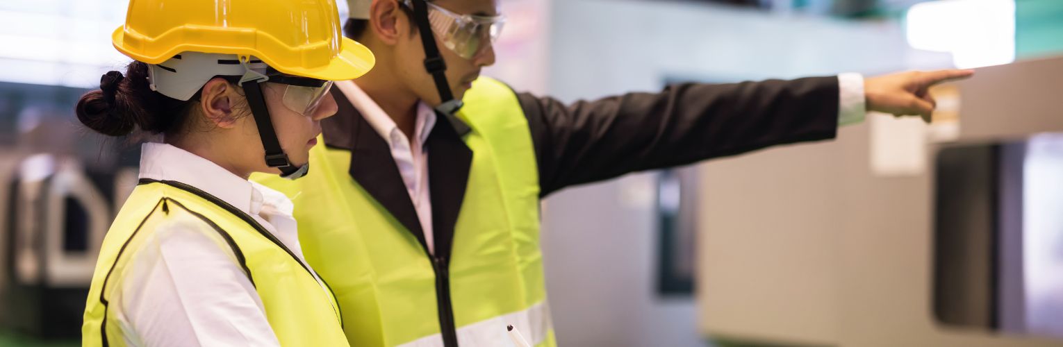 Waist up female factory worker write implement audit result of industrial machine while manager point finger to machinery. Manufacturing industry to produce car spare parts.