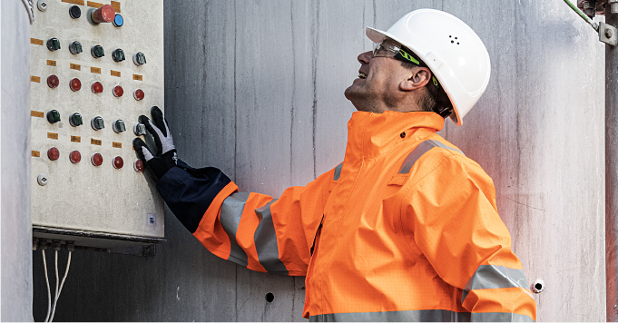 A man wearing PPE looking at a switch board